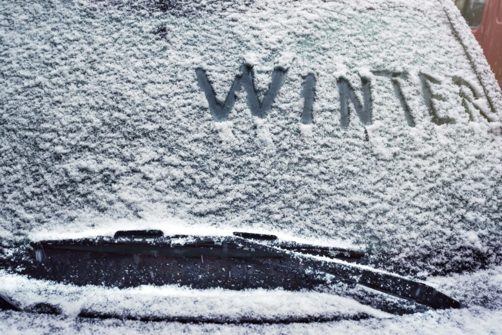 Picture of wind shield with snow on it spelling out the word "Winter".